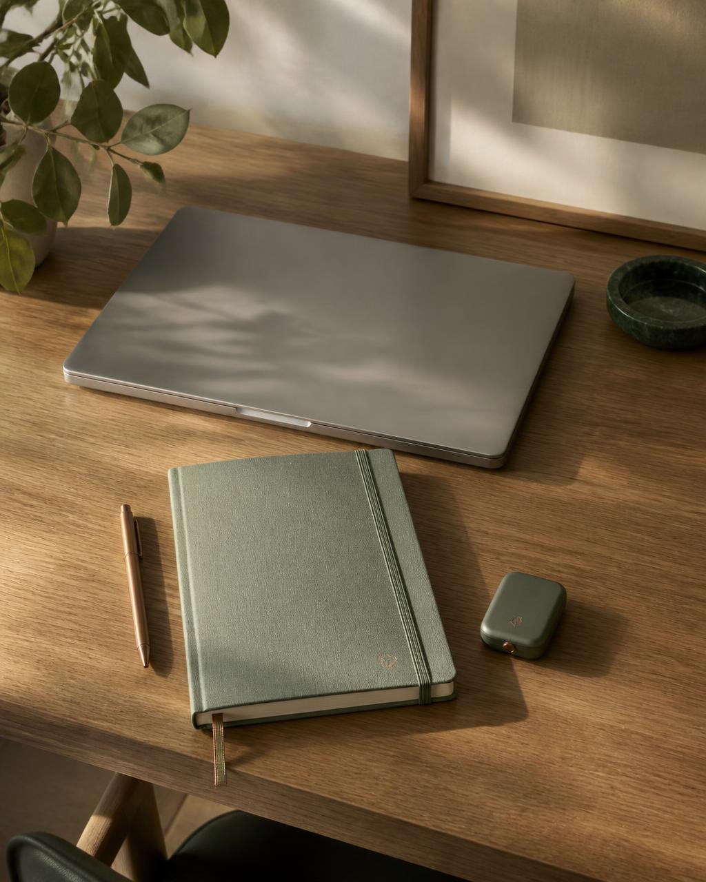 A minimal technology stack with one laptop, notebook, and pen on a warm oak desk